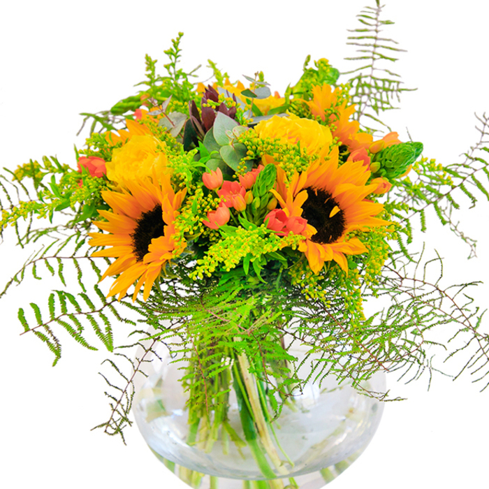 This sun-drenched bouquet, crafted by an expert Tooting florist, radiates optimism and heartfelt connection. At its core are exuberant sunflowers whose velvety ochre petals and dark centers seem to channel the joyful hum of Tooting Market. Woven beside them, garden roses in decadent yellow unfold petal by petal, each swirl illuminated like morning light filtering onto a quiet street off Mitcham Road. Scarlet hypericum berries add a dash of character-playful and bold-contrasting sharply with the surrounding mellow yellows and deep greens. Wisps of fern, delicate solidago sprigs with gold-dusted tips, and slender vertical greens introduce movement that echoes the gentle breeze one might feel wandering past Tooting Bec Lido on a summer afternoon. Bluish eucalyptus, with its muted hues, fills out the backdrop, instilling a sense of natural calm. All of these are arranged within a crystal-clear, rounded vase-modern in silhouette and timeless in appeal-where water and tidy stems glisten together, embodying freshness and intention. The bouquet's energetic texture, harmonious palette, and understated sophistication make it the perfect companion for special Tooting occasions: whether a birthday, anniversary, or simply bringing cheer to a cozy Balham home. Designed with care in Tooting, this arrangement stands as an emblem of local warmth, contemporary style, and unwavering floral craftsmanship.